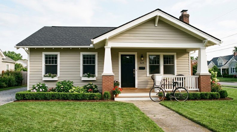 Light greige bungalow with white trim, black door, brick porch columns, and bicycle in Louisville KY